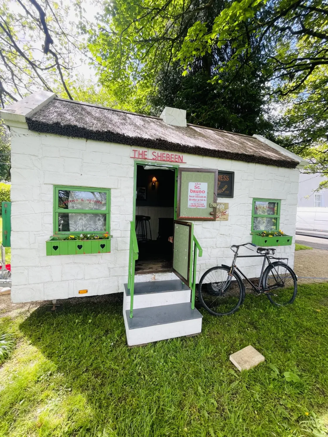 A small white cottage with green trim and a bicycle outside.