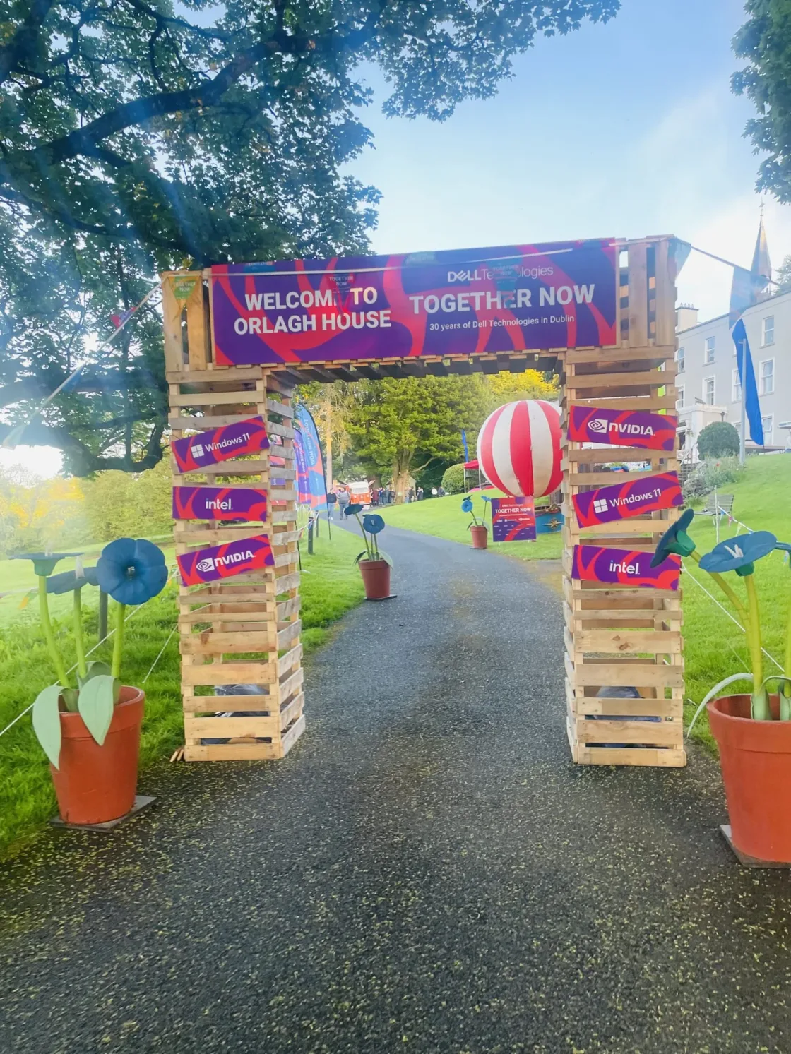 A colourful outdoor welcome arch leading towards a decorated event lawn.