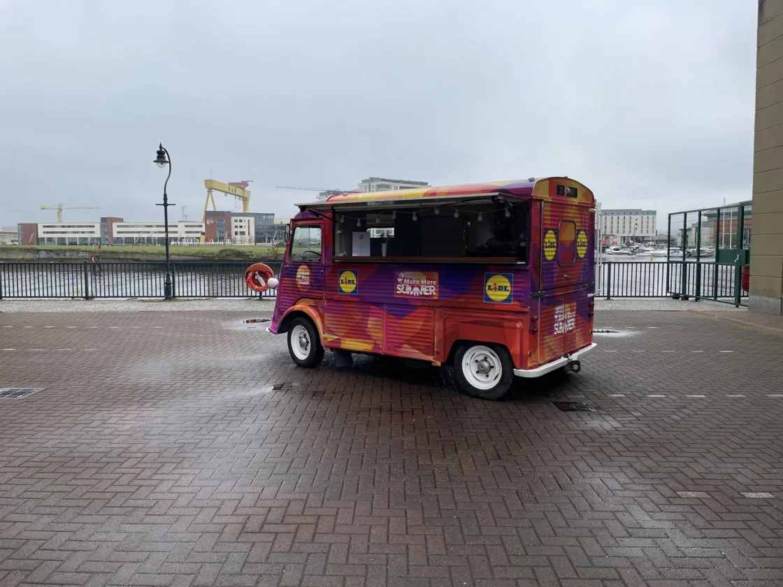A colourful catering van with its serving hatch open beside the waterfront.