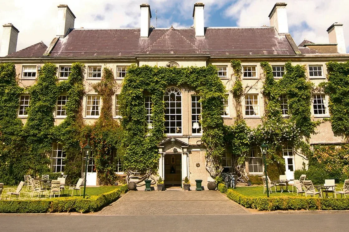 An ivy-covered country house with a central entrance and formal planting.