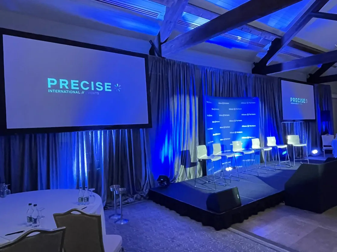 A PRECISE presentation screen beside a conference stage lit in blue.