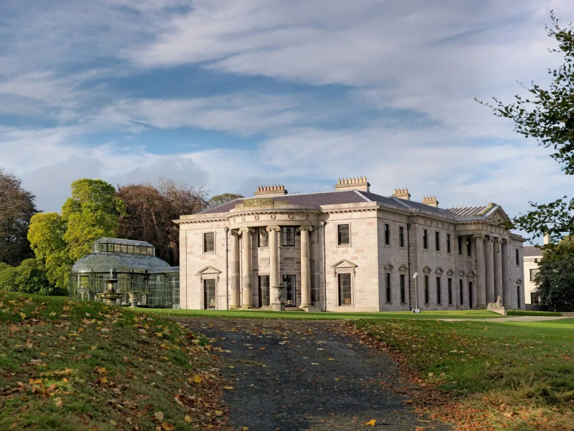 A stone country house with columns, lawns and mature trees.