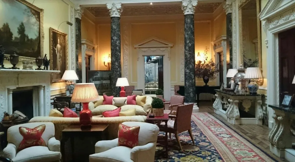 A grand drawing room with columns, paintings and upholstered seating.