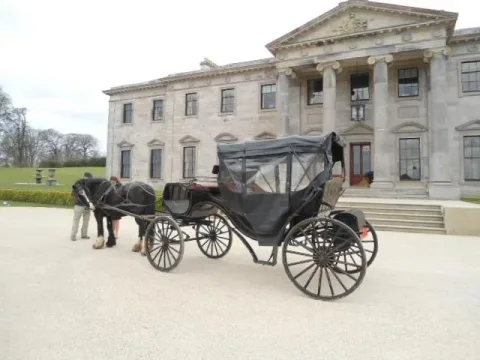 A horse-drawn carriage outside a columned country house.
