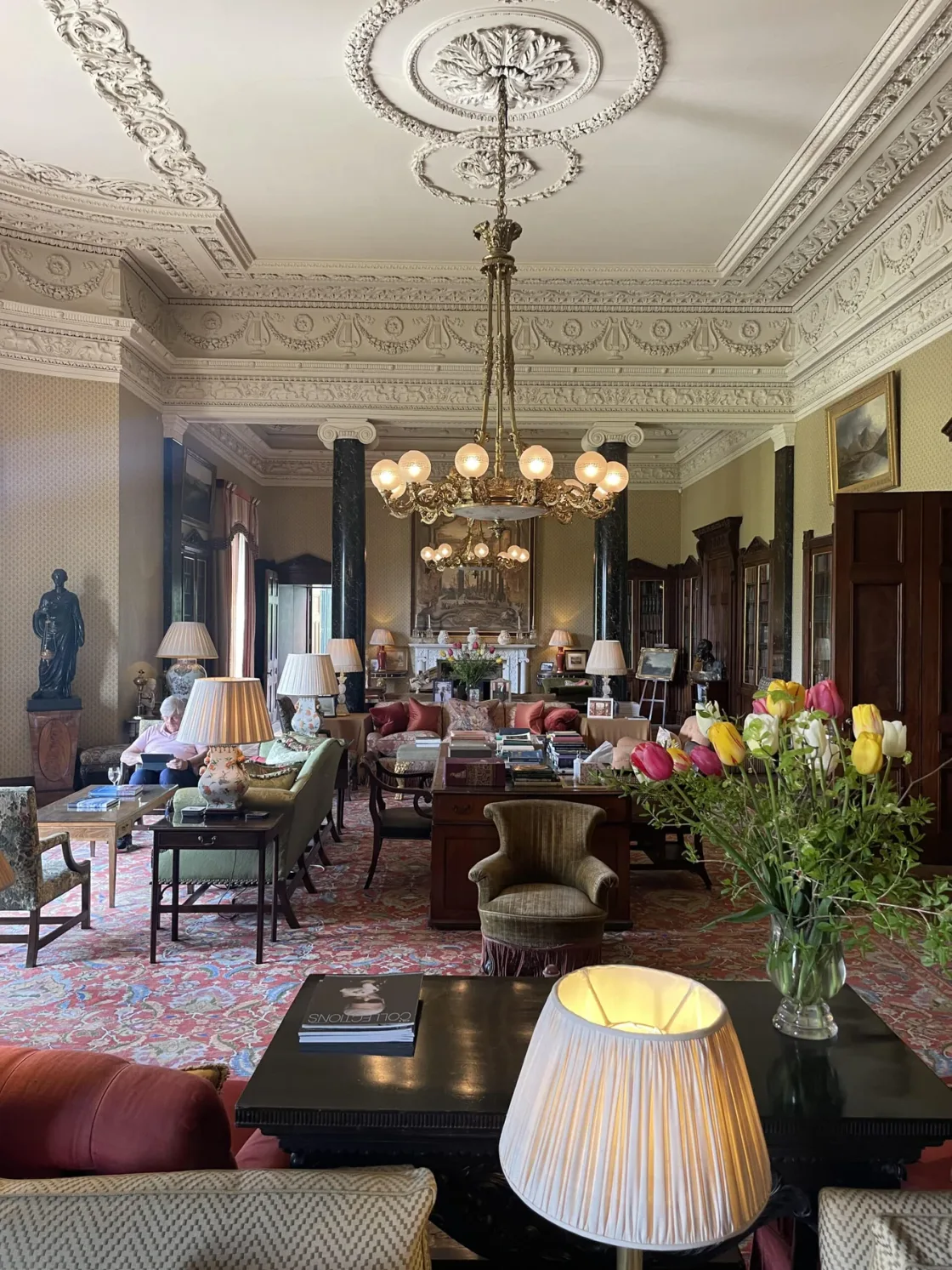 A long drawing room with an ornate ceiling, chandeliers and lounge seating.