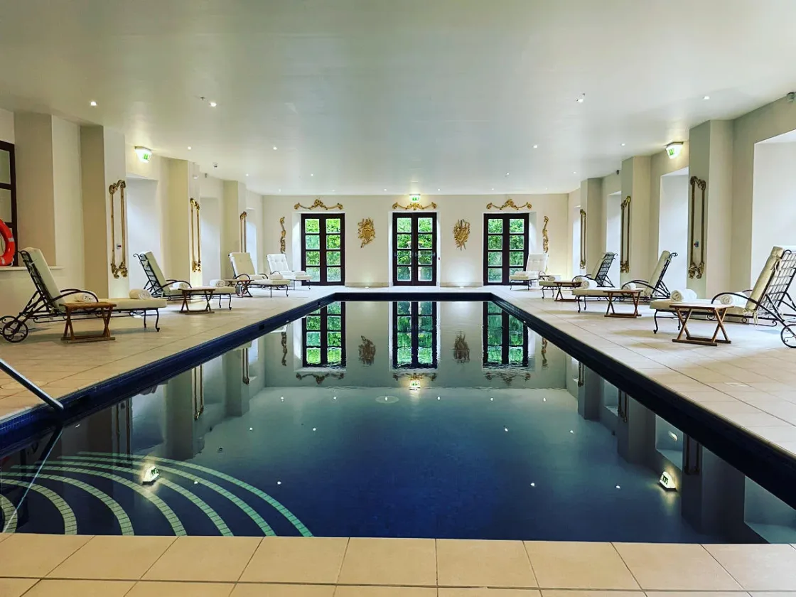 An indoor swimming pool with loungers and tall windows.