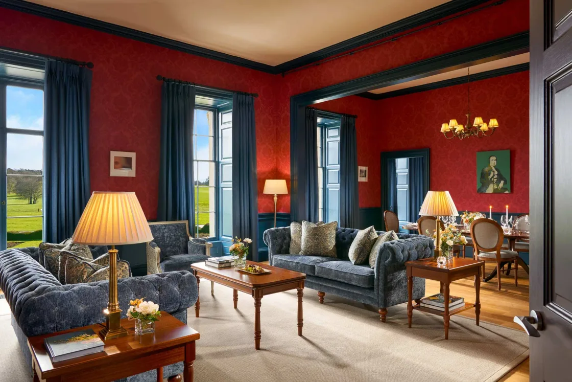 A red-panelled sitting room with lamps and upholstered chairs.
