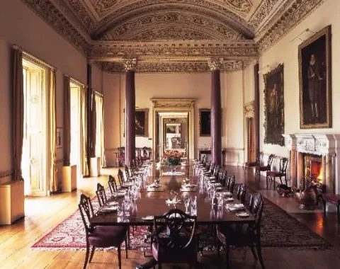 A long dining table beneath an ornate ceiling and portrait paintings.