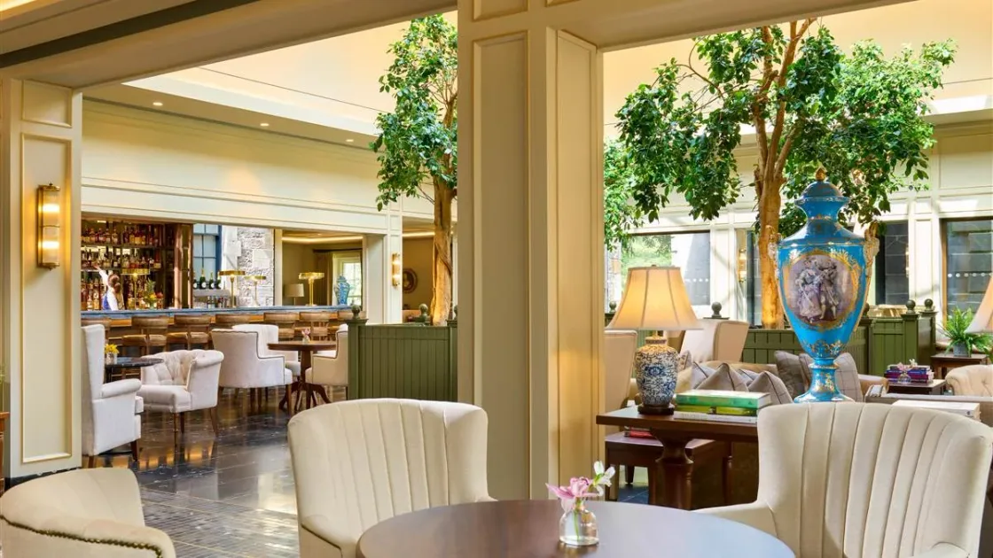 A bright dining room with cream furniture, flowers and indoor greenery.