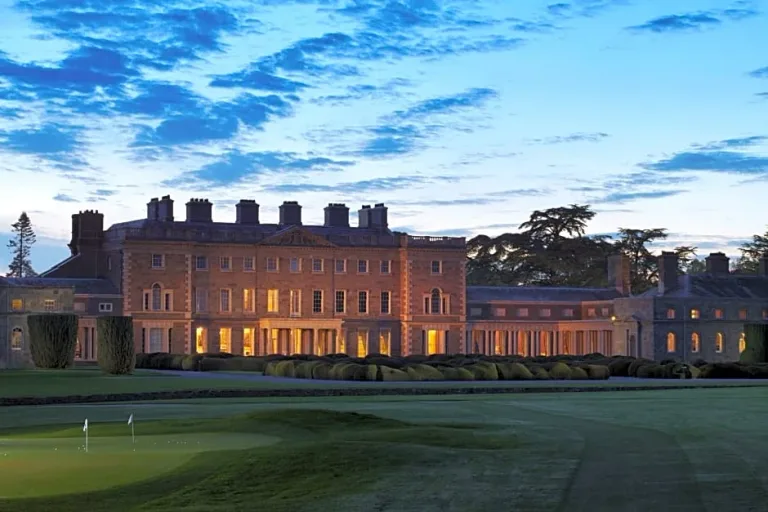 A country house illuminated at dusk beyond a wide lawn.
