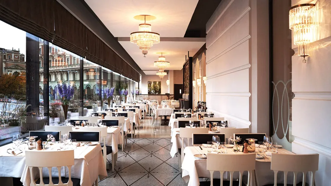 A bright restaurant with dining tables beside tall windows.