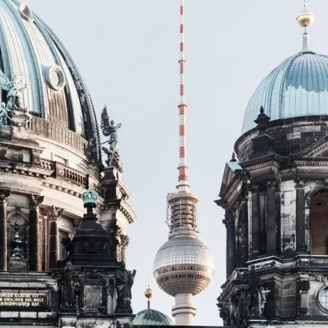 A television tower seen between the domes of historic city buildings.