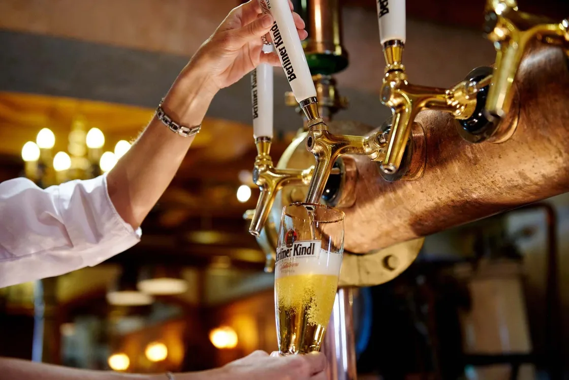 A drink being poured from a brass tap into a tall glass.