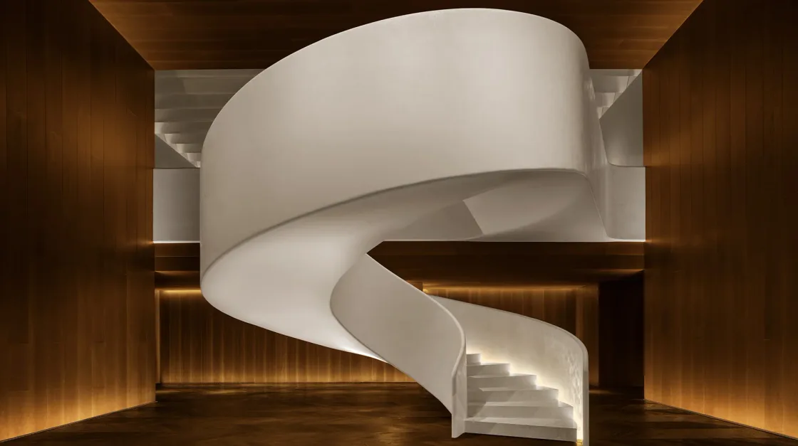 A sculptural white spiral staircase inside a dark timber interior.