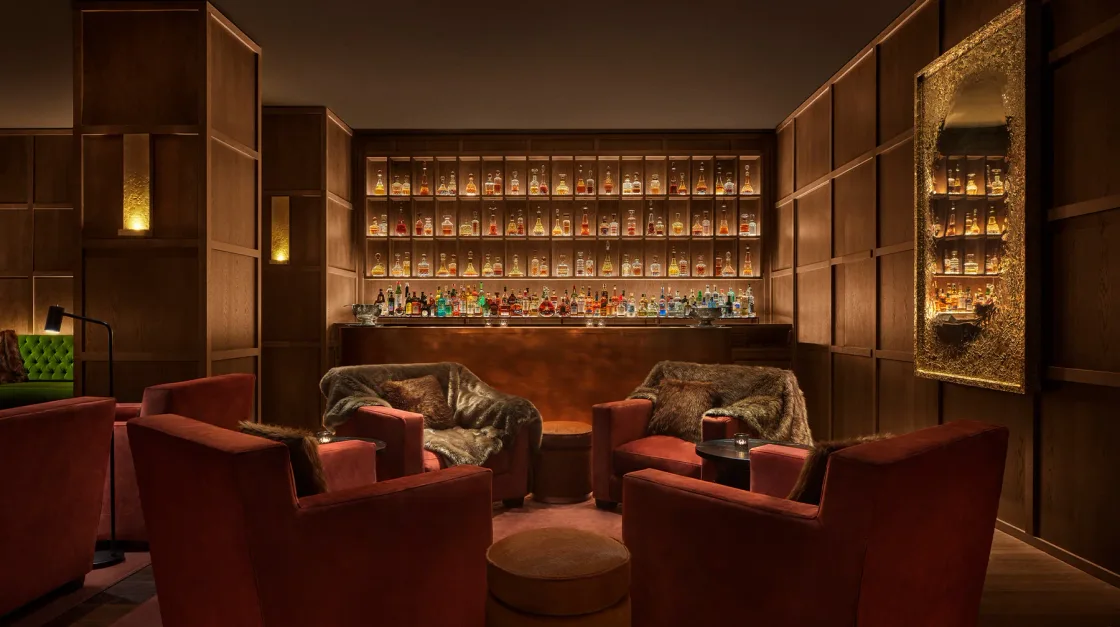 A warmly lit lounge with red armchairs and shelves of bottles.