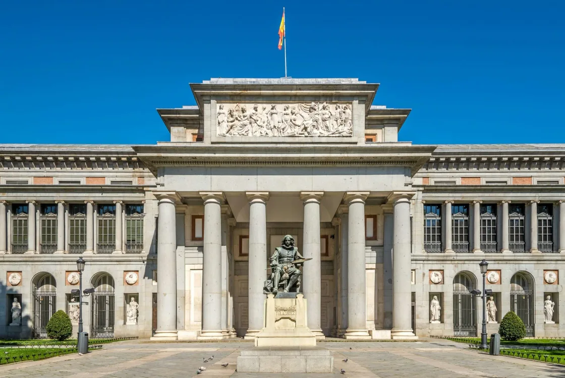 The columned facade of a large museum beneath a clear blue sky.