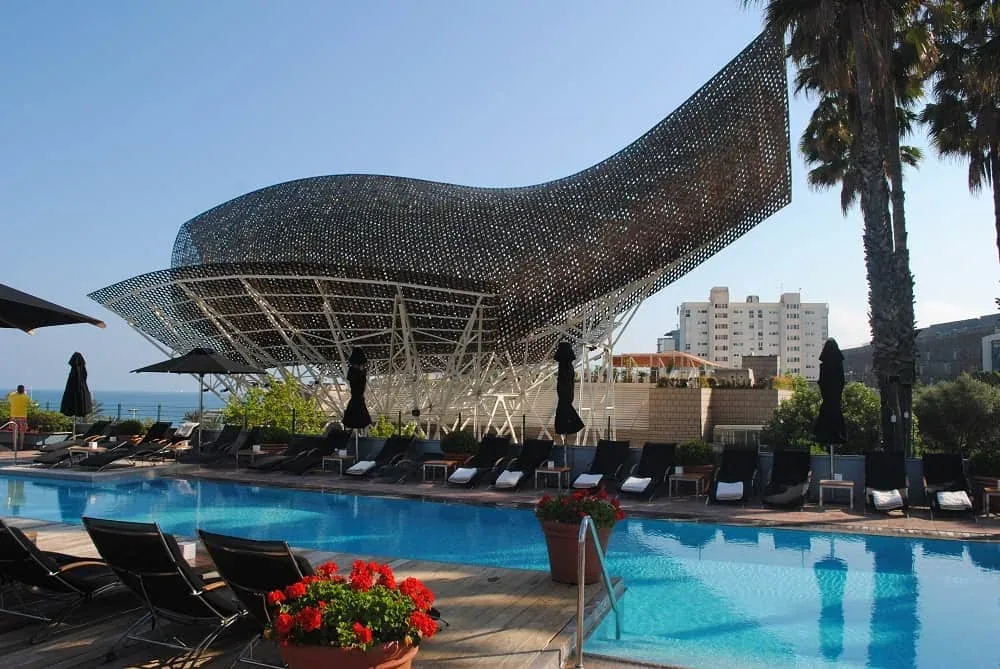 Poolside loungers beneath a large curved metal sculpture.