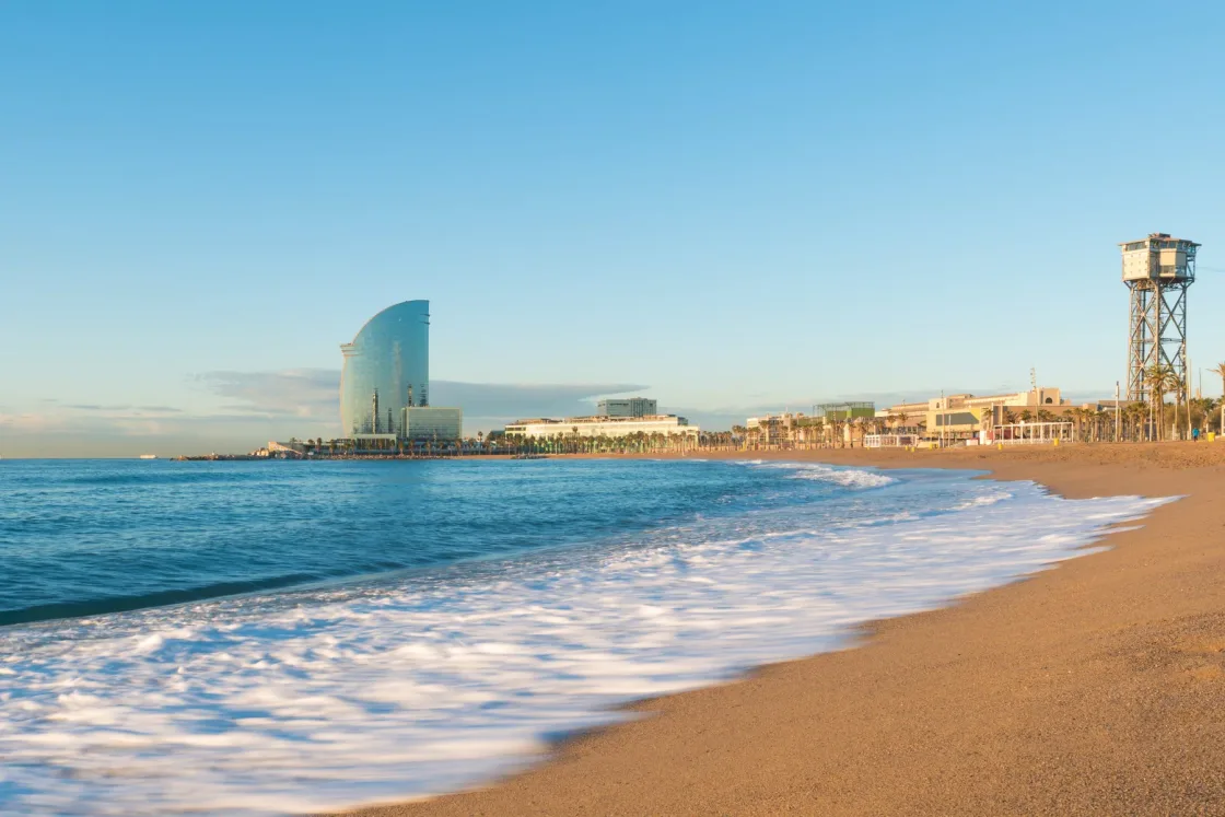 Waves breaking along a sandy city beach beside a curved glass tower.