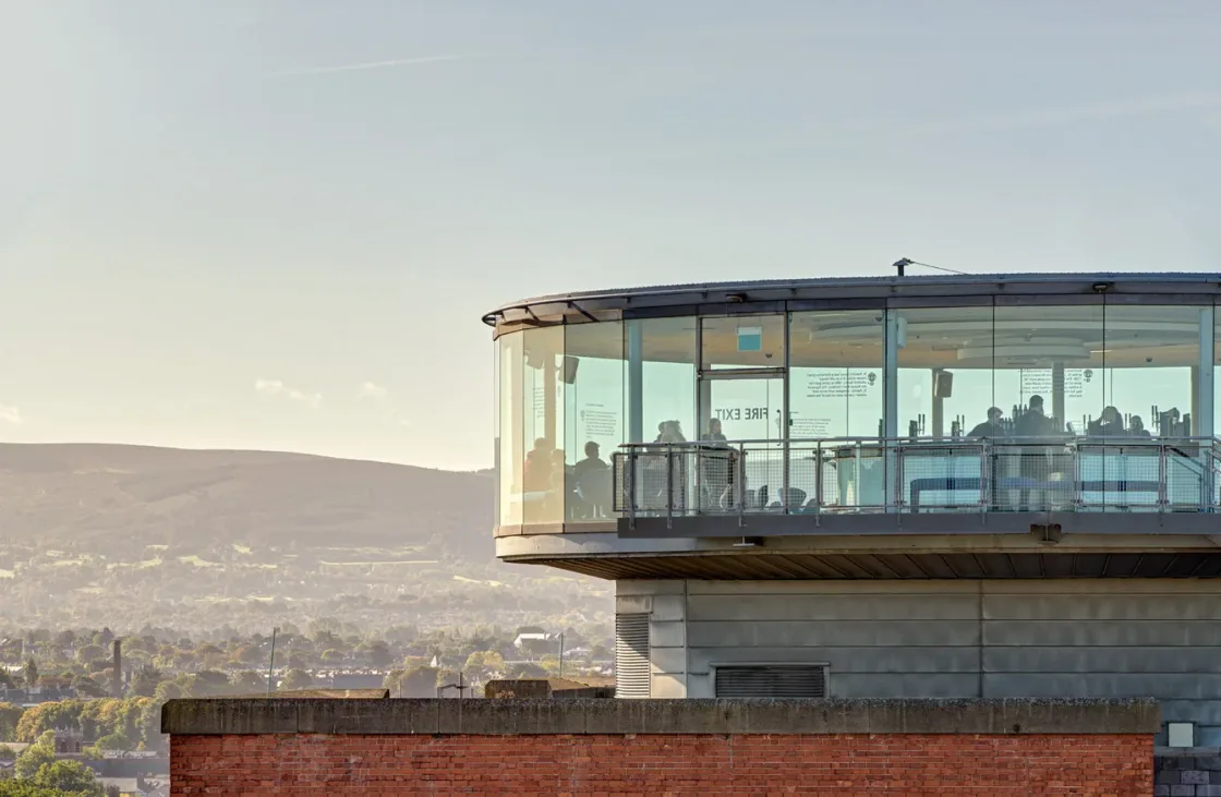 A glass-walled rooftop room overlooking the city and distant hills.
