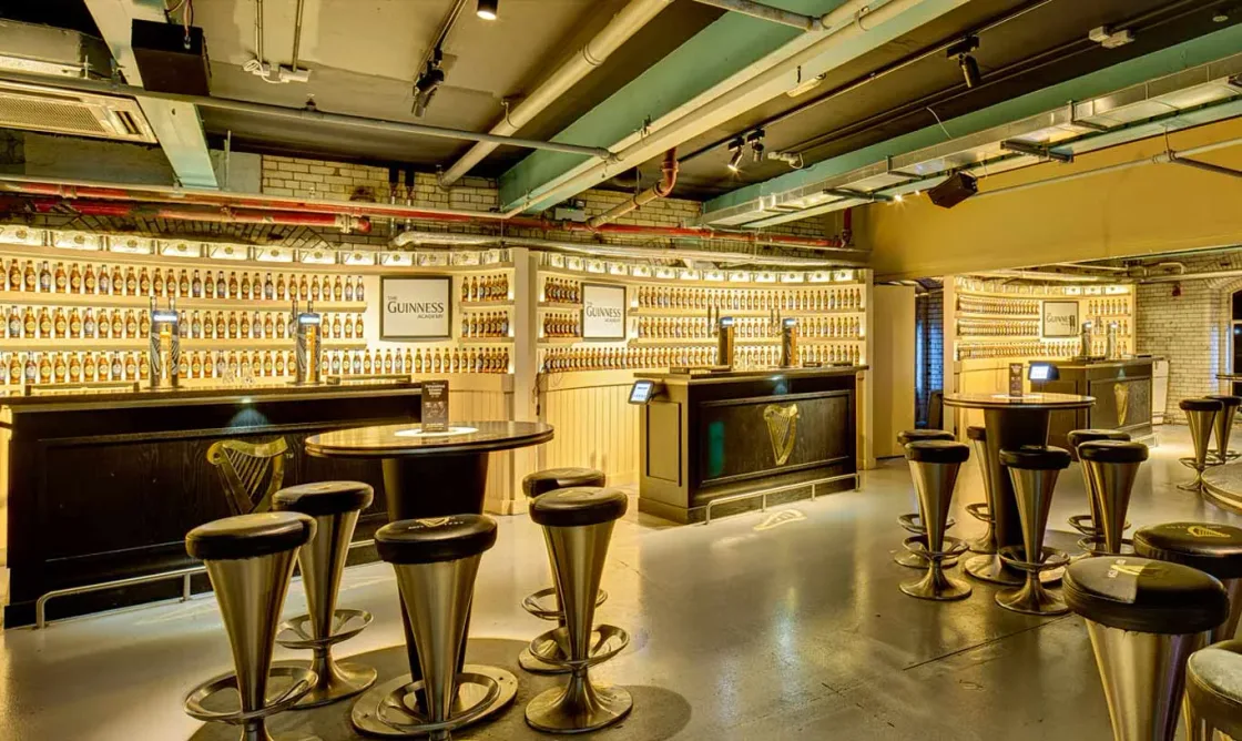 An illuminated bar lined with high stools and shelves of glassware.