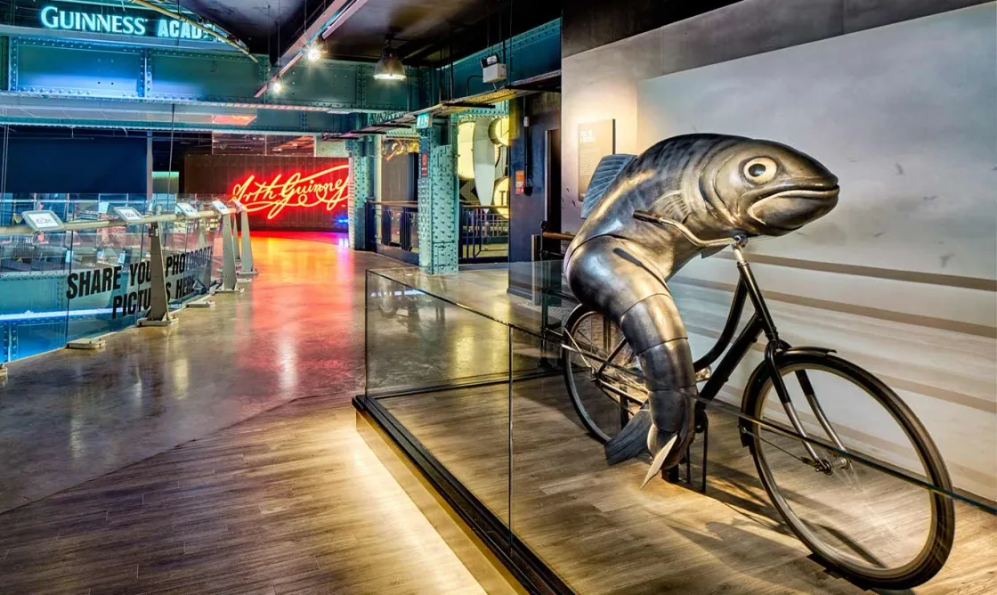 An indoor display featuring a large sculpted fish riding a bicycle.
