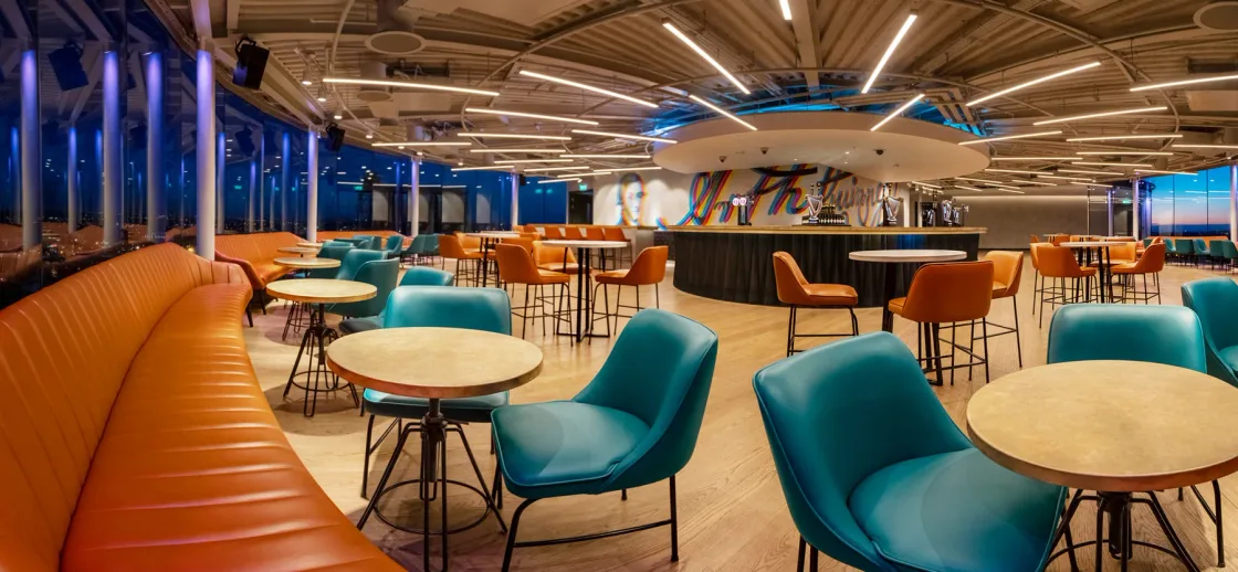 A bright restaurant with turquoise chairs, orange banquettes and an exposed ceiling.