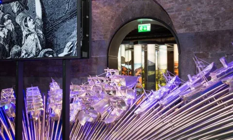A transparent sculptural display inside a brick-vaulted museum gallery.