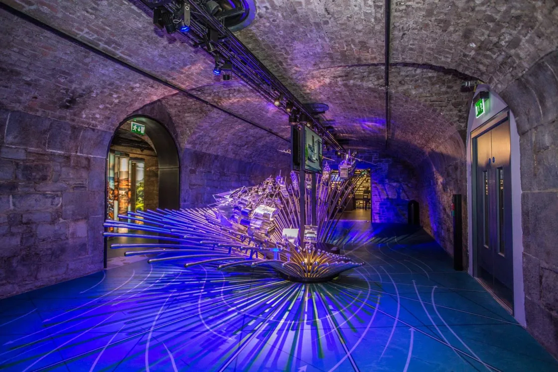 Purple-and-blue lighting around a sculpture in a brick-vaulted room.