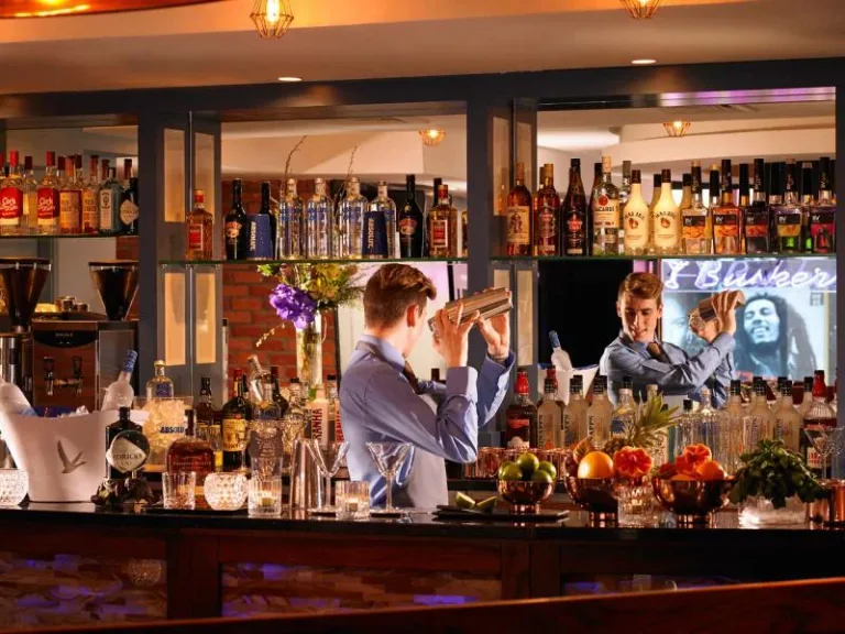 A bartender behind a counter lined with bottles and flowers.
