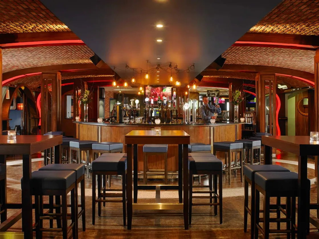 A warmly lit bar with chandeliers and high tables.