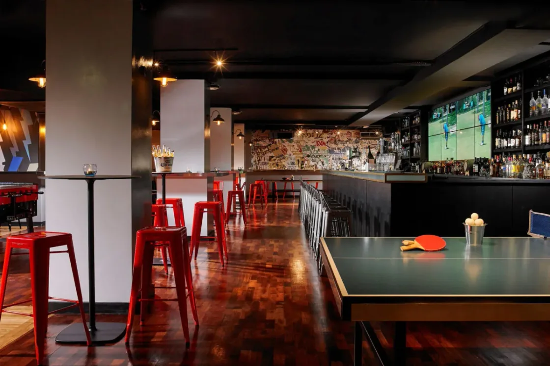 A bar interior with high red stools, table seating and television screens.