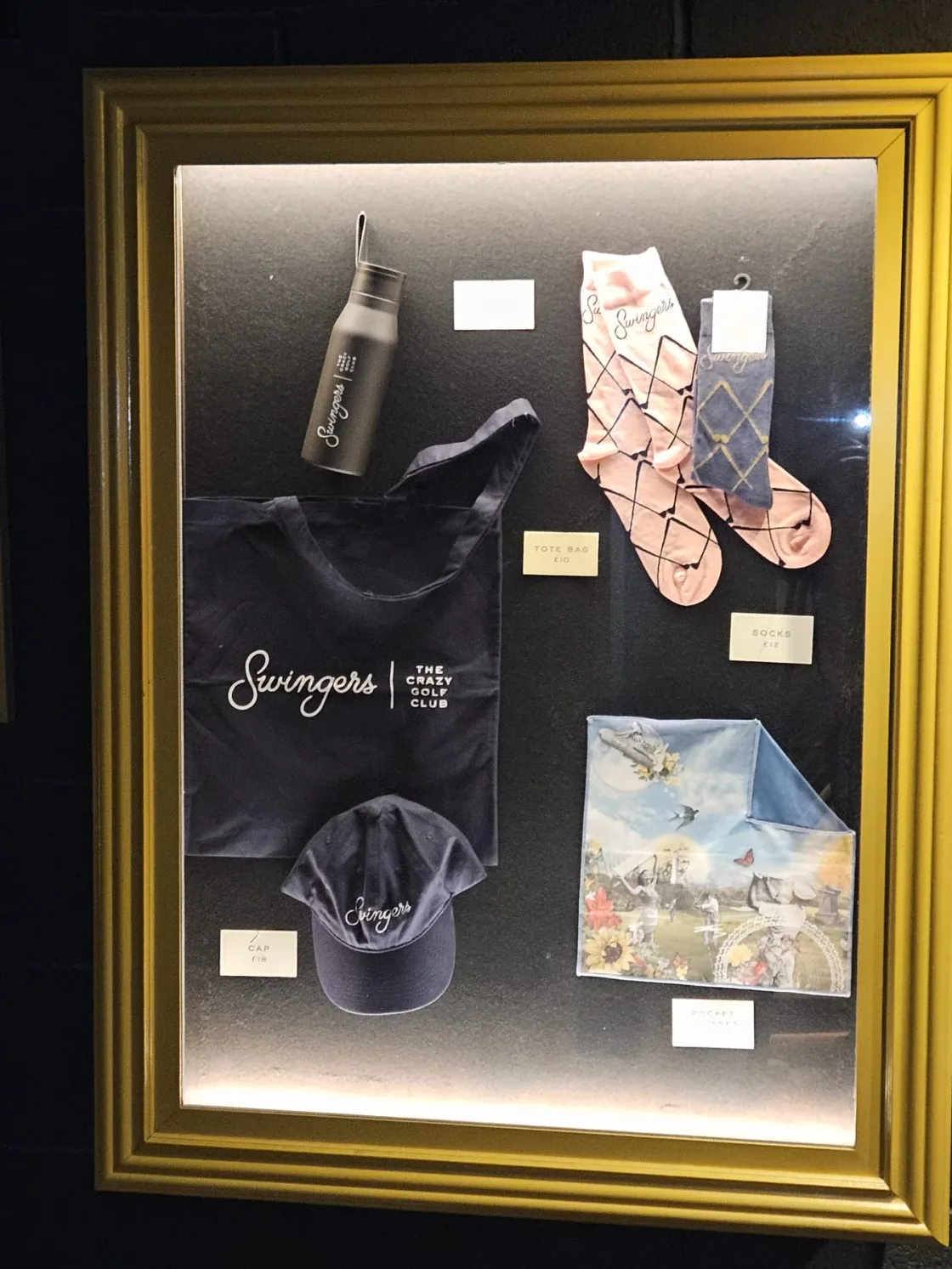 A gold-framed display of small objects and printed cards.