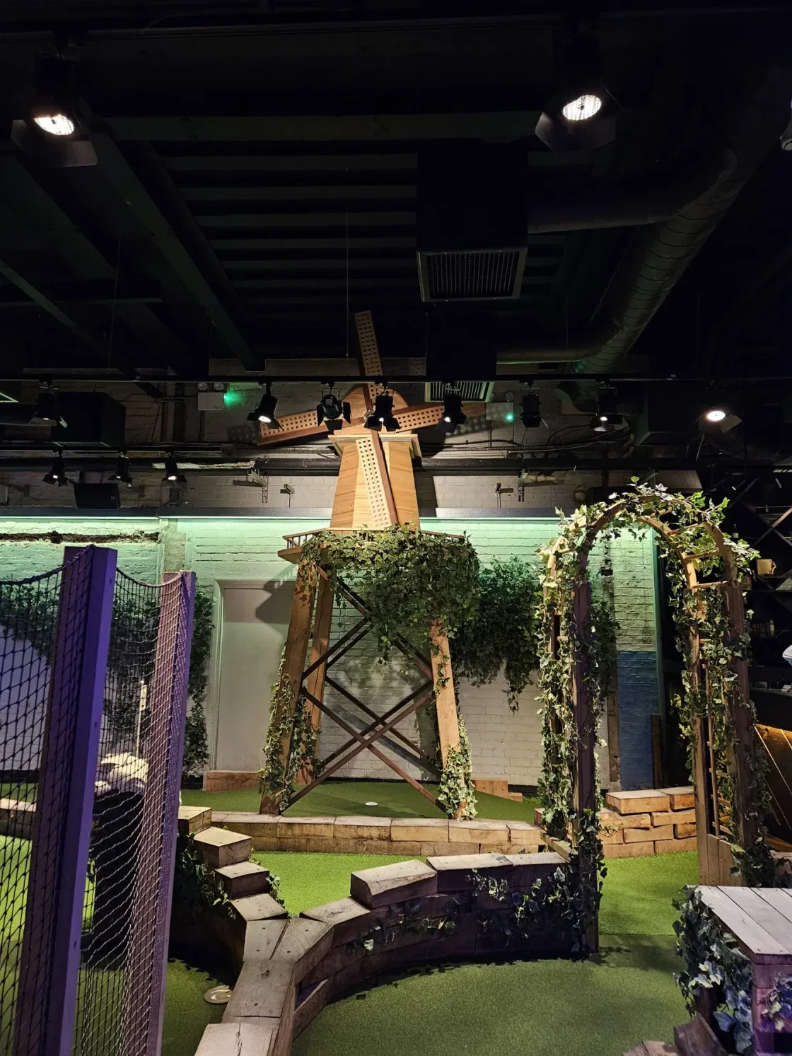An indoor mini-golf course decorated with greenery and timber structures.