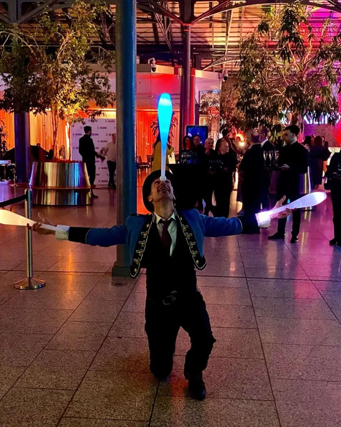 Guests in a venue decorated with suspended foliage and colourful lighting.
