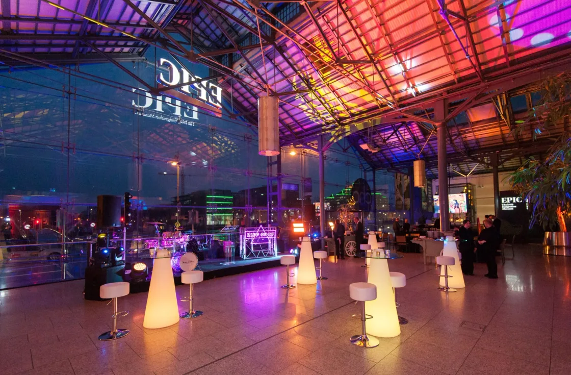An event hall with a glazed roof, illuminated cocktail tables and colourful lighting.