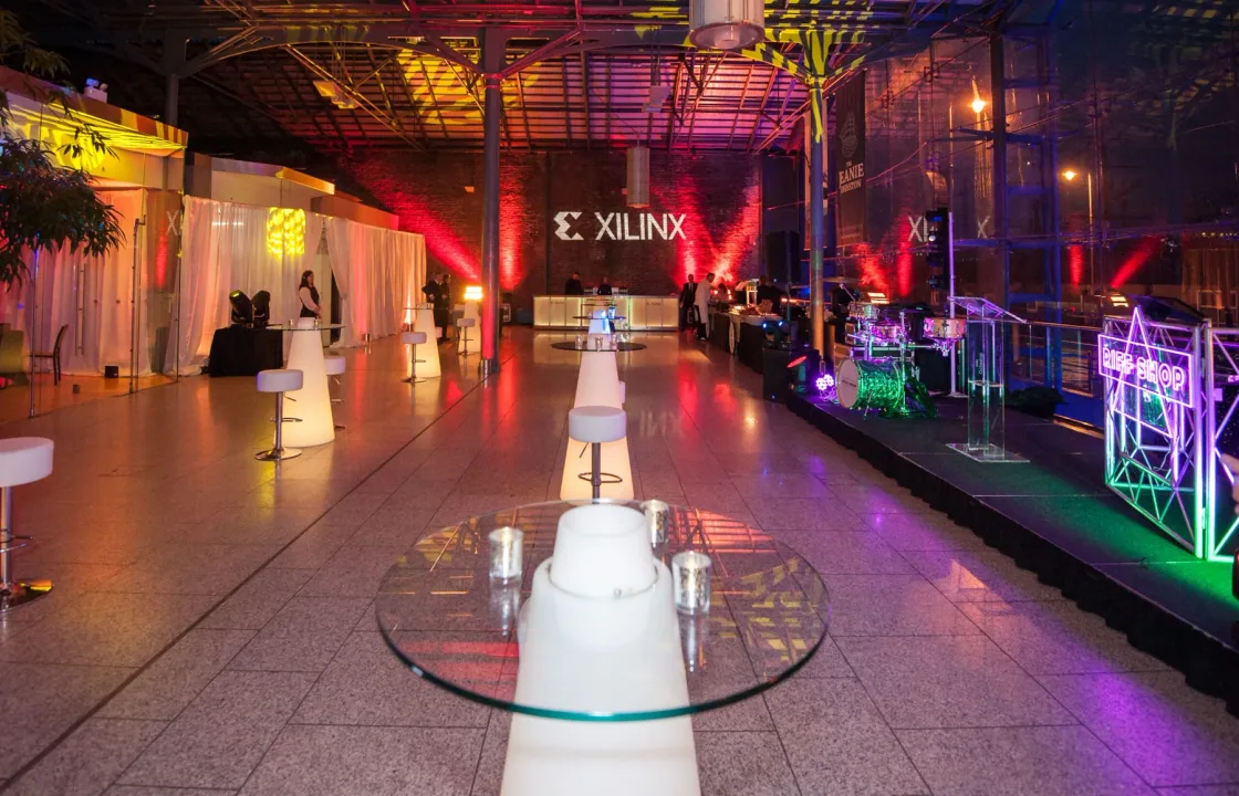 A colourful event hall with cocktail tables and an illuminated bar.