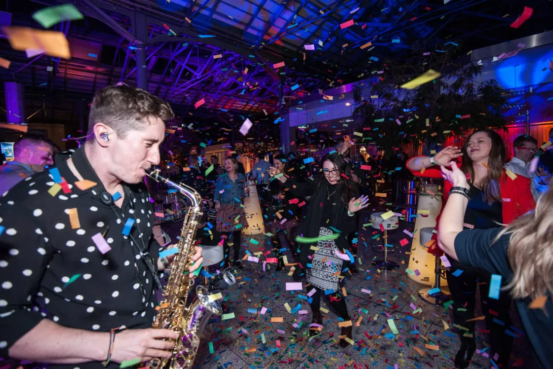 A saxophonist performing among guests and falling confetti.